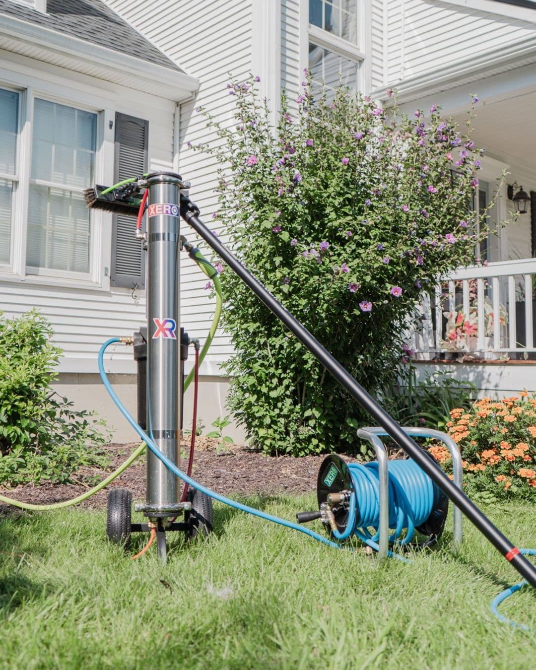 XERO pure water window cleaning system and blue hose reel on a residential lawn.