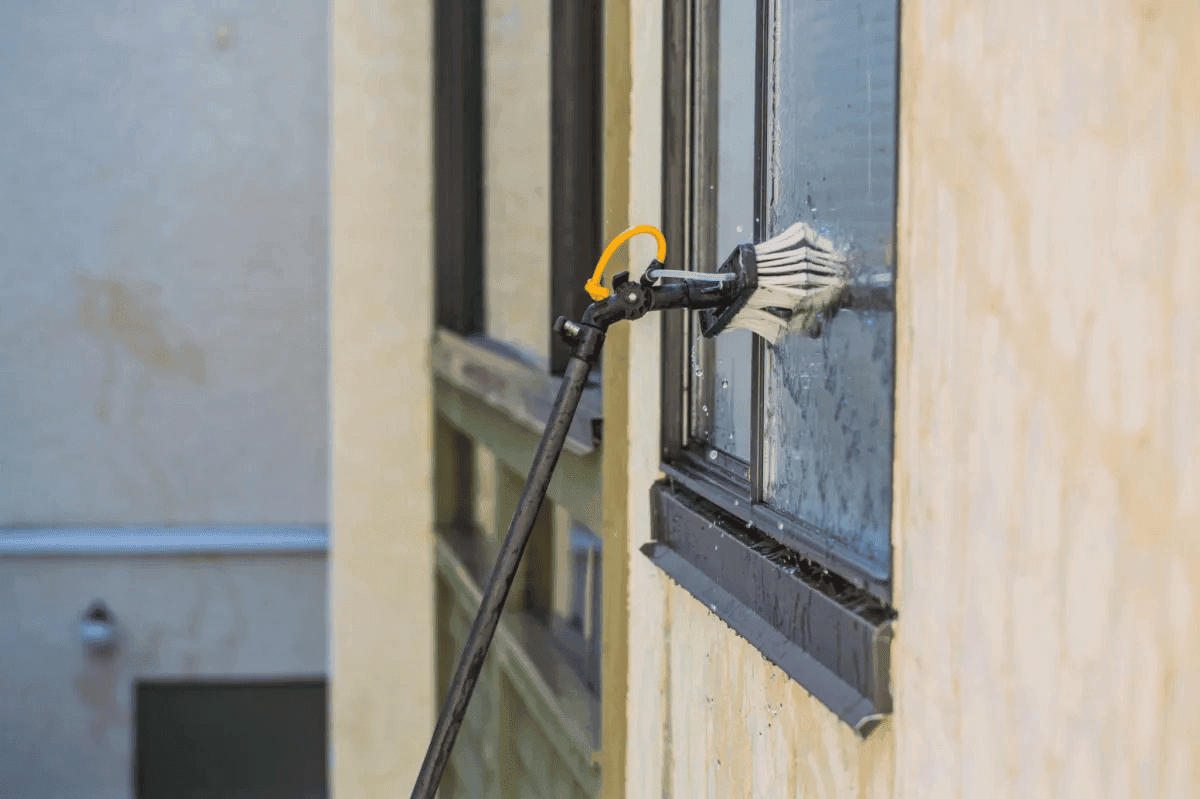 A water-fed pole brush cleaning a glass window on a light-colored building exterior.